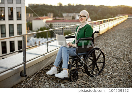 Muslim lady with disability working on laptop outdoors Muslim lady with disability working on laptop outdoors 104339532