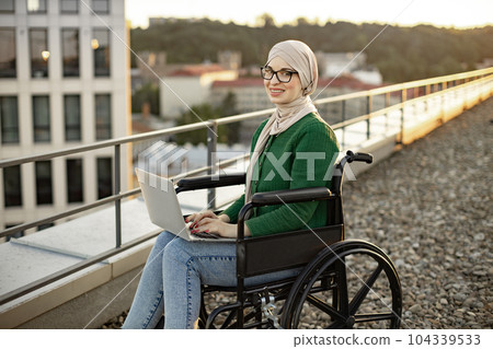 Business lady in wheelchair with laptop posing on terrace Business lady in wheelchair with laptop posing on terrace 104339533