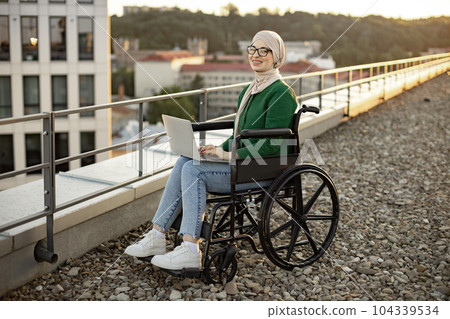 Muslim lady with disability working on laptop outdoors Muslim lady with disability working on laptop outdoors 104339534