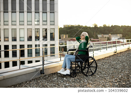 Person in headscarf sitting in wheelchair outside in morning 104339602