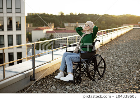 Person in headscarf sitting in wheelchair outside in morning 104339603