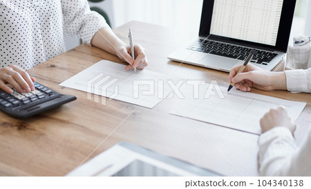 Two accountants using a laptop computer and calculator while counting taxes at wooden desk in office. Teamwork in business audit and finance 104340138