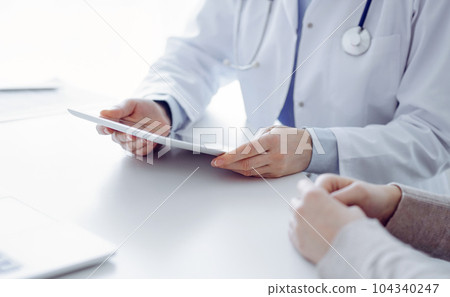 Doctor and patient sitting at the table in clinic while using tablet computer. The focus is on female patient's hands, close up. Medicine concept 104340247