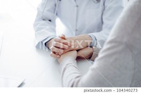 Doctor and patient sitting at the table in clinic office. The focus is on female physician's hands reassuring woman, only hands close up. Medicine concept 104340273