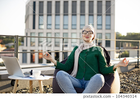 Adult in hijab meditating in bean bag in rooftop workplace Adult in hijab meditating in bean bag in rooftop workplace 104340314