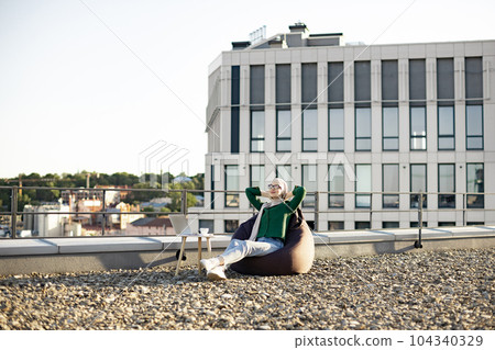 Muslim person lazing in pouf chair on terrace in spring Muslim person lazing in pouf chair on terrace in spring 104340329