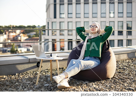 Lady in headscarf relaxing in bean bag on roof terrace Lady in headscarf relaxing in bean bag on roof terrace 104340330