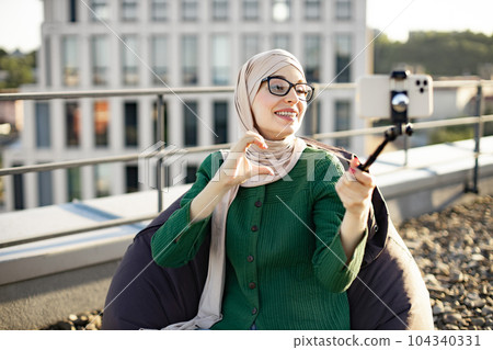Adult in hijab showing heart sign on mobile outdoors 104340331