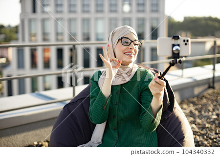 Muslim woman with phone on stick filming content on rooftop Muslim woman with phone on stick filming content on rooftop 104340332