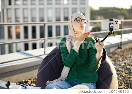 Person sending air kiss via phone on selfie stick outdoors Person sending air kiss via phone on selfie stick outdoors 104340333