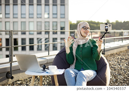 Muslim woman with phone on stick filming content on rooftop Muslim woman with phone on stick filming content on rooftop 104340337