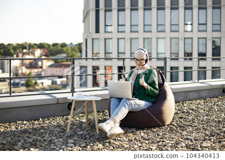 Woman in hijab running web conference via devices on rooftop Woman in hijab running web conference via devices on rooftop 104340413