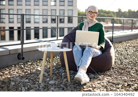 Muslim employee with gadget doing remote job on rooftop Muslim employee with gadget doing remote job on rooftop 104340492