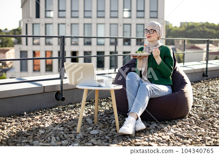 Woman in hijab on lunch break during remote work on rooftop Woman in hijab on lunch break during remote work on rooftop 104340765