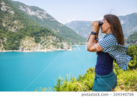 Young woman using binoculars exploring the nature at the Piva lake in Montenegro Young woman using binoculars exploring the nature at the Piva lake in Montenegro 104340786