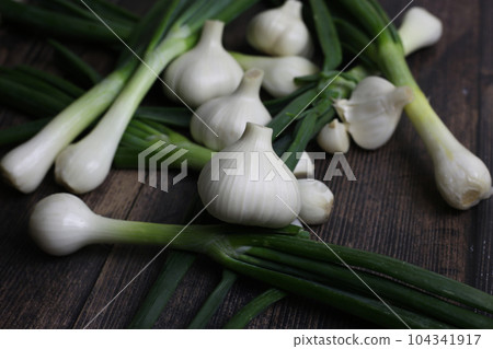 Fresh garlic and onions on the table. Kitchen still life with heads of garlic. Vegetables ingredients for a recipe on a kitchen board Fresh garlic and onions on the table. Kitchen still life with heads of garlic. Vegetables ingredients for a recipe on a kitchen board 104341917
