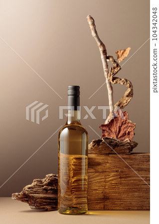Bottle of white wine with a composition of old plank, dry snags, and dried vine leaves. 104342048