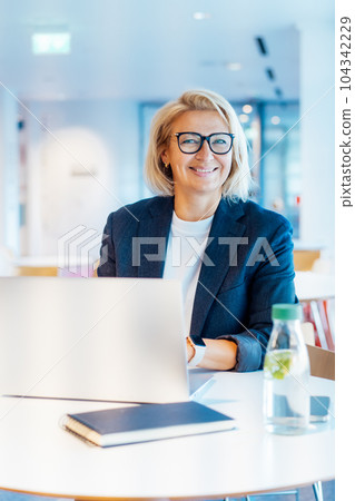 Portrait of 50's confident mature businesswoman looking at camera, middle-aged experienced senior female professional working on laptop in open space office. Female entrepreneur working remotely. Portrait of 50's confident mature businesswoman looking at camera, middle-aged experienced senior female professional working on laptop in open space office. Female entrepreneur working remotely. 104342229