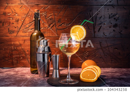 Bar composition. A beautiful wine glass with an orange slice and a straw. Shaker and wine with cork. 104343238