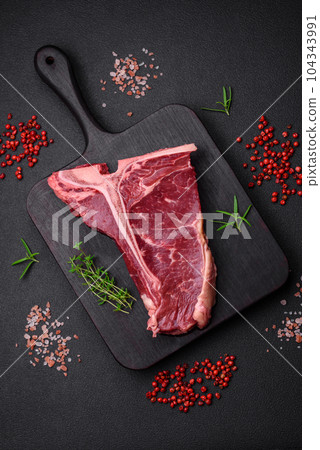 Raw juicy beef t-bone steak with salt, spices and herbs 104343991