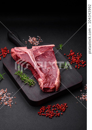 Raw juicy beef t-bone steak with salt, spices and herbs 104343992