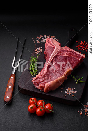 Raw juicy beef t-bone steak with salt, spices and herbs 104343999