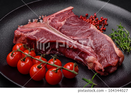 Raw juicy beef t-bone steak with salt, spices and herbs 104344027