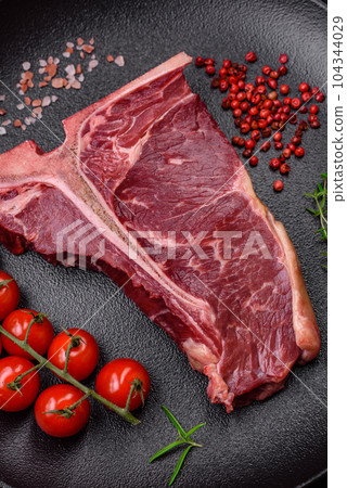 Raw juicy beef t-bone steak with salt, spices and herbs 104344029