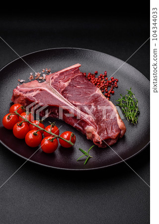 Raw juicy beef t-bone steak with salt, spices and herbs 104344033