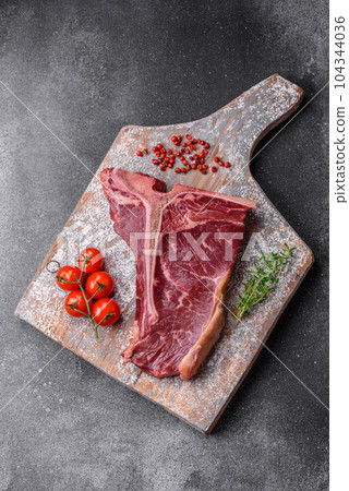 Raw juicy beef t-bone steak with salt, spices and herbs 104344036