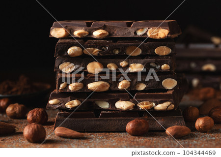 Dark and milk chocolate with nuts on a dark background sprinkled with cocoa powder. Dark and milk chocolate with nuts on a dark background sprinkled with cocoa powder. 104344469