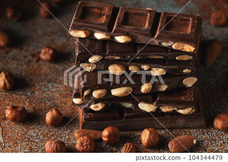Dark and milk chocolate with nuts on a dark background sprinkled with cocoa powder. Dark and milk chocolate with nuts on a dark background sprinkled with cocoa powder. 104344479