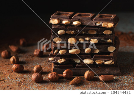 Dark and milk chocolate with nuts on a dark background sprinkled with cocoa powder. 104344481
