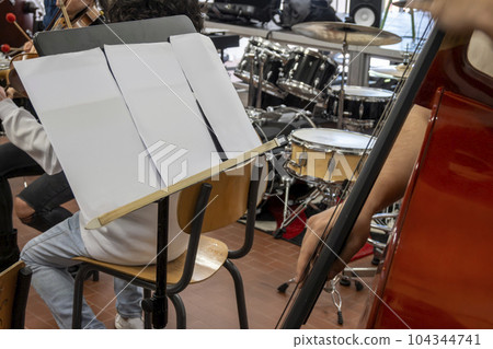 Real life young music students during rehearsals. Musical instruments and music stand with stave. Real life young music students during rehearsals. Musical instruments and music stand with stave. 104344741
