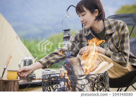 A young woman relaxing in front of a bonfire outdoor solo camping chairing A young woman relaxing in front of a bonfire outdoor solo camping chairing 104348080