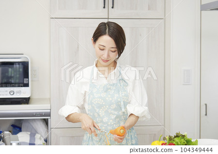 Middle aged woman peeling carrots with a peeler in the kitchen 104349444
