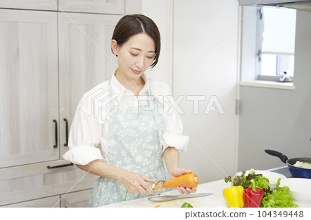 Middle aged woman peeling carrots with a peeler in the kitchen 104349448