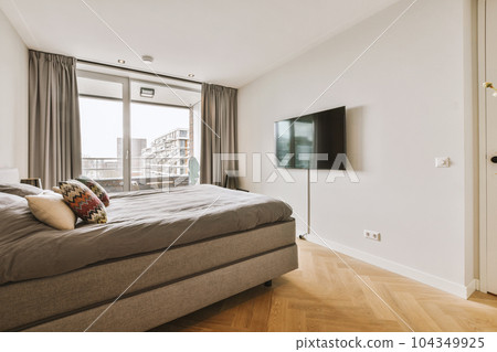 a bedroom with wood flooring and white walls, there is a flat screen mounted tv on the wall above the bed a bedroom with wood flooring and white walls, there is a flat screen mounted tv on the wall above the bed 104349925