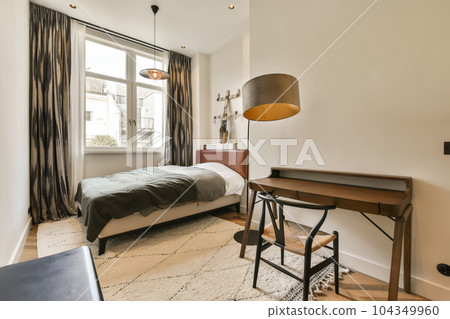 a bedroom with a bed, desk and window in the middle of the room there is a lamp on top of the headboard a bedroom with a bed, desk and window in the middle of the room there is a lamp on top of the headboard 104349960