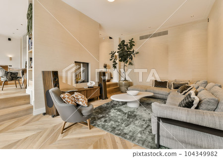 a living room with wood flooring and beige wallpapers on the walls there is a couch, coffee table, two chairs a living room with wood flooring and beige wallpapers on the walls there is a couch, coffee table, two chairs 104349982