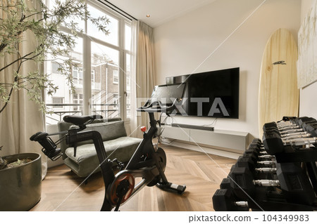 a living room with an exercise bike in front of the window and a television set up on the wall behind it 104349983