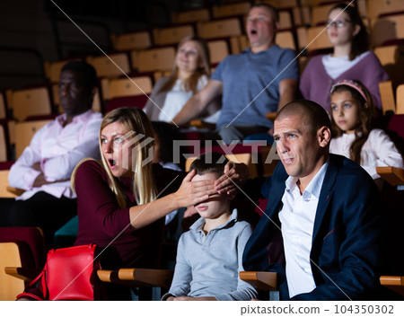 mother, father and their son sitting at scary perfomance in theatrical auditorium 104350302