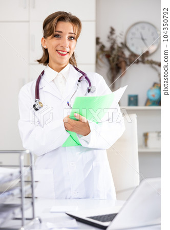Smiling woman doctor holding paper folder and looking at camera 104350792