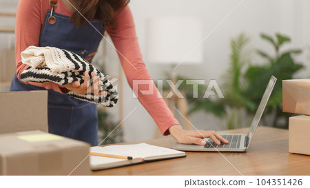 Online shopping business concept, Women entrepreneur checks order on laptop and pack clothes in box Online shopping business concept, Women entrepreneur checks order on laptop and pack clothes in box 104351426
