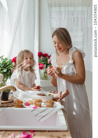 A little blonde girl with her mom on a kitchen countertop decorated with peonies. The concept of the relationship between mother and daughter. Spring atmosphere. A little blonde girl with her mom on a kitchen countertop decorated with peonies. The concept of the relationship between mother and daughter. Spring atmosphere. 104354905