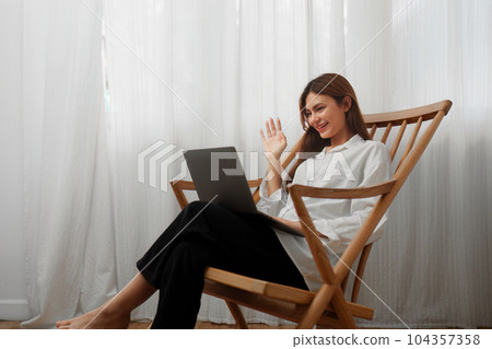 Portrait of a young cheerful asian woman sitting rocking chair and using laptop computer at home Portrait of a young cheerful asian woman sitting rocking chair and using laptop computer at home 104357358