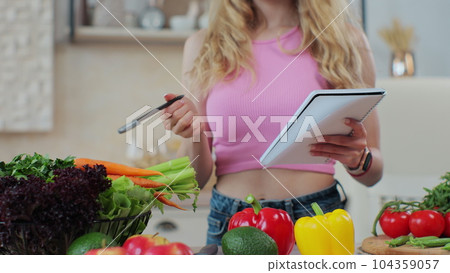 Close up of woman in the kitchen checking a shopping list on a notebook at home. Healthcare concept. Organic fresh fruit and vegetables. Dieting Concept. 104359057