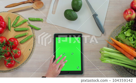 Young woman scrolls through recipes on her tablet in the kitchen. Application for cooking. Healthy food concept. Young woman scrolls through recipes on her tablet in the kitchen. Application for cooking. Healthy food concept. 104359142