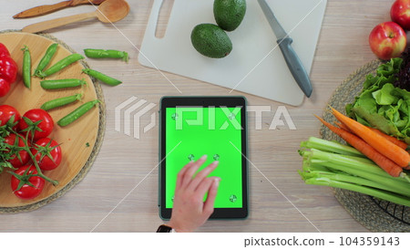 Woman scrolls through recipes on her tablet in the kitchen. Application for cooking. Healthy food concept. Woman scrolls through recipes on her tablet in the kitchen. Application for cooking. Healthy food concept. 104359143