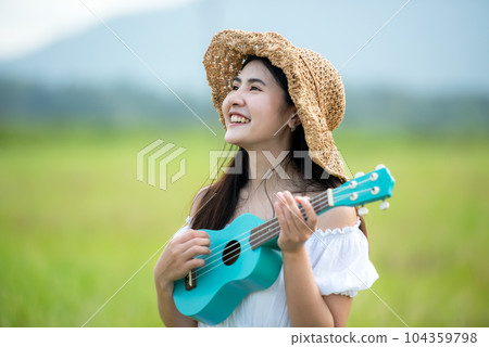 Lifestyle asian women white dress holding a guitar on a cloudy sunrise sky in the meadow flower, Lifestyle asian women white dress holding a guitar on a cloudy sunrise sky in the meadow flower, 104359798
